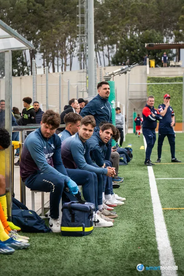 Soccer team bench with players and coaches on a field.