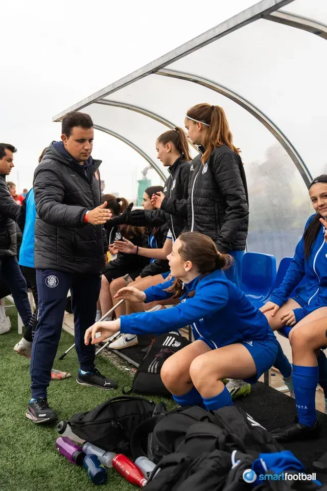 Soccer coach talking to female players on the bench during a game.