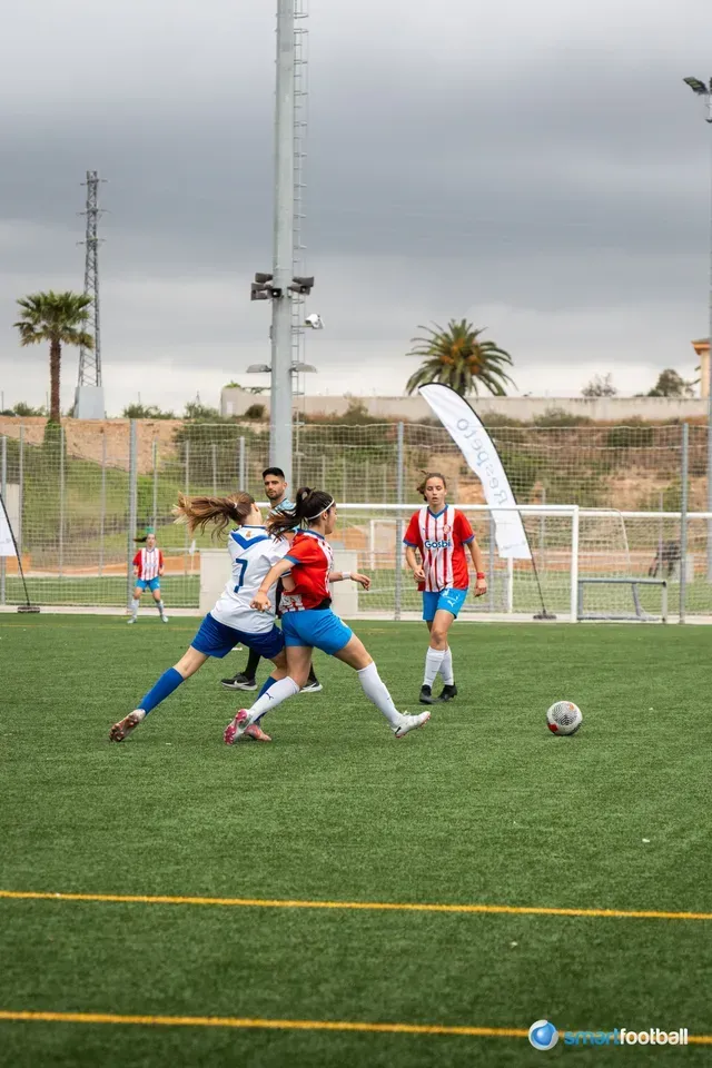 Two women in soccer uniforms compete for the ball on a green field.