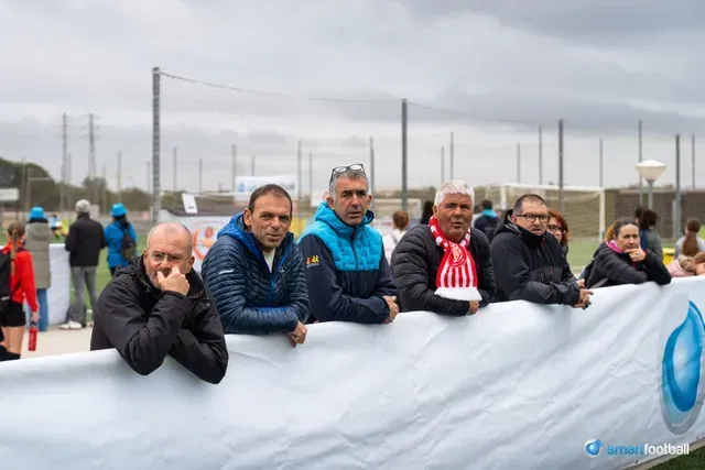 Soccer fans watch a game from behind a banner on a cloudy day.