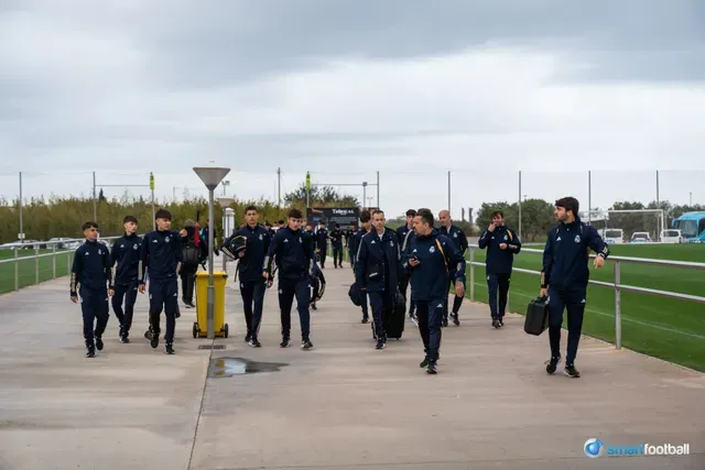 Soccer team walking together on a pathway, wearing dark blue uniforms, outdoors on a cloudy day.