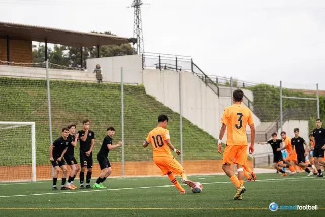 Soccer player in orange jersey kicking a free kick towards the goal, with a wall of black-clad players.