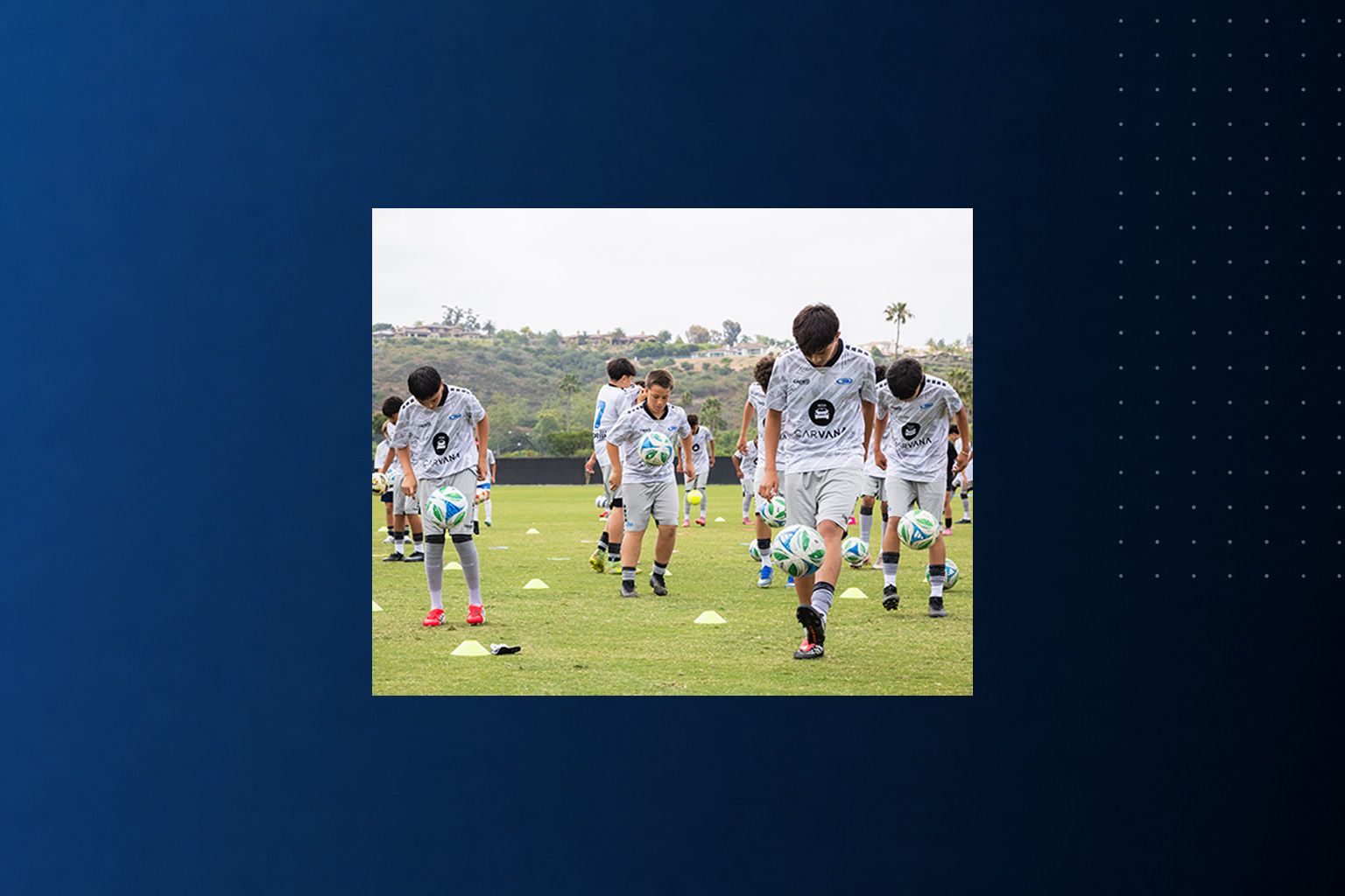 Soccer players warming up on a grassy field in white training kits under an overcast sky