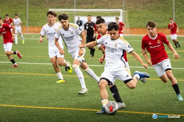 Soccer players in white and red uniforms on a green field, one kicking the ball.
