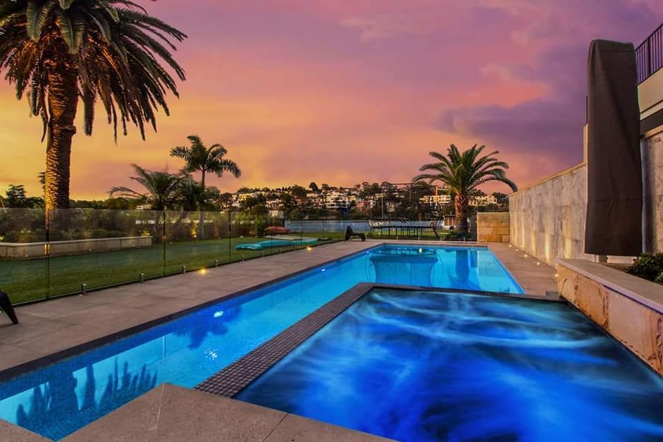 A large swimming pool with palm trees in the background at sunset — Dimension One Glass Fencing In Newcastle, NSW