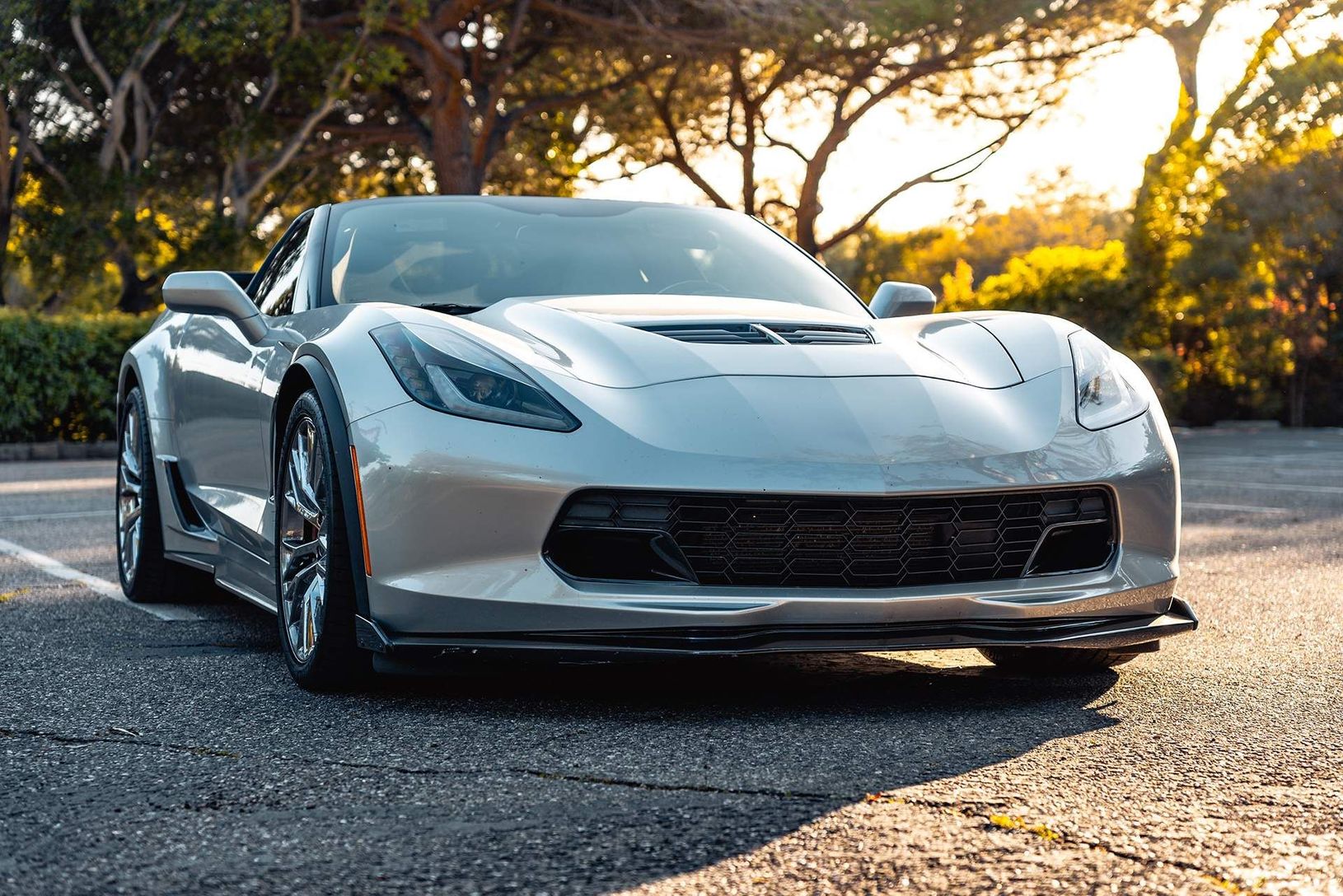 Silver sports car parked on a road at sunset, with trees and golden light in the background