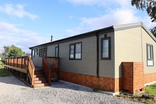 Gray mobile home with a wooden porch and steps on a gravel lot