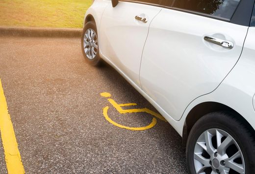 White car parked in a handicapped parking space, showing a yellow wheelchair symbol on the pavement