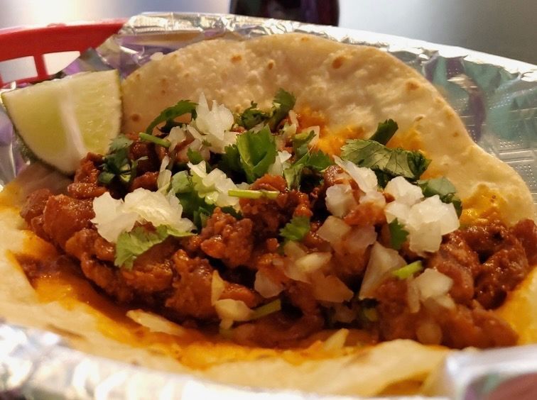 Taco with meat, cilantro, and onions on a soft tortilla, served with a lime wedge.