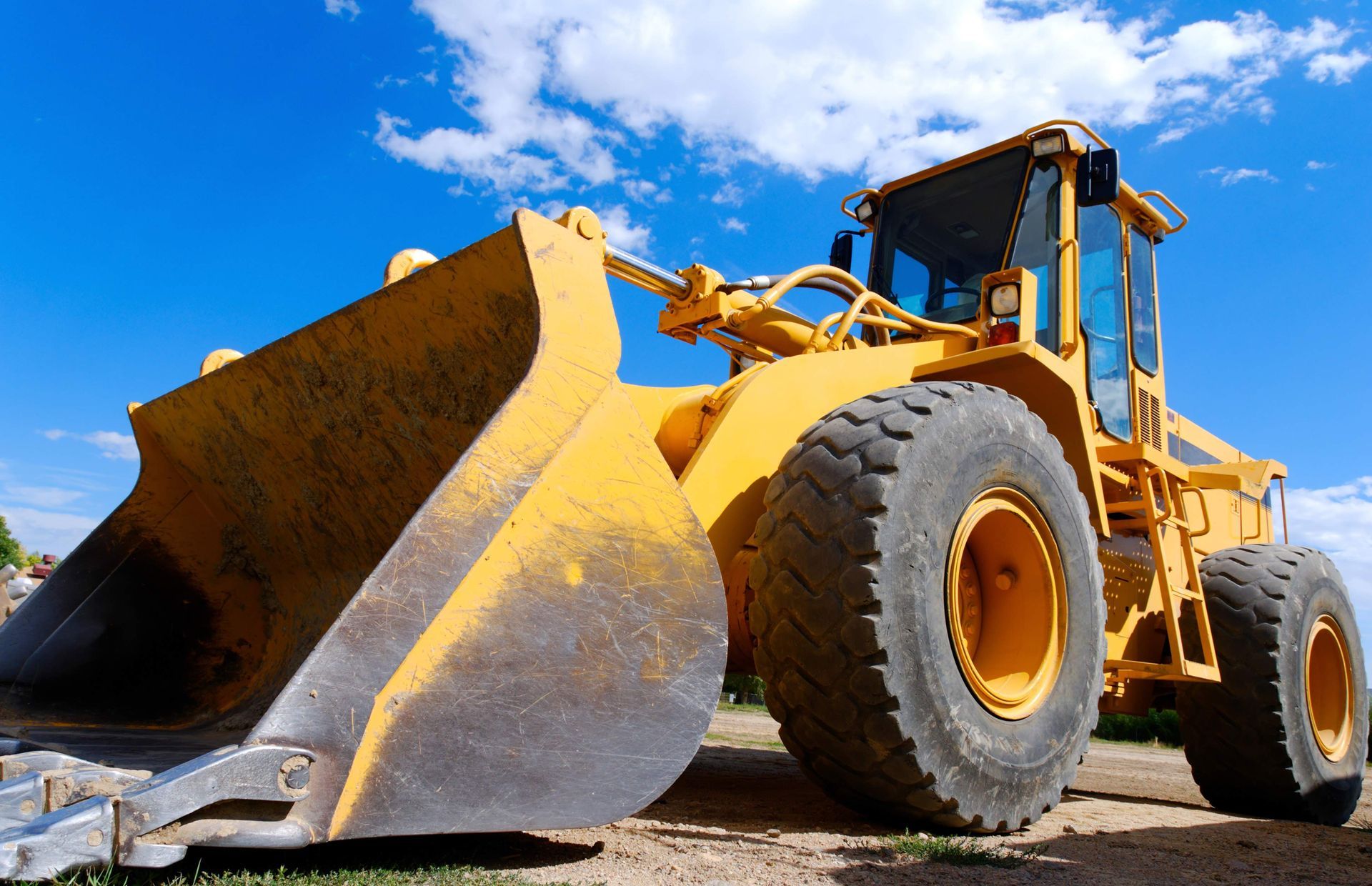 A yellow bulldozer with a large bucket is parked on a dirt road.