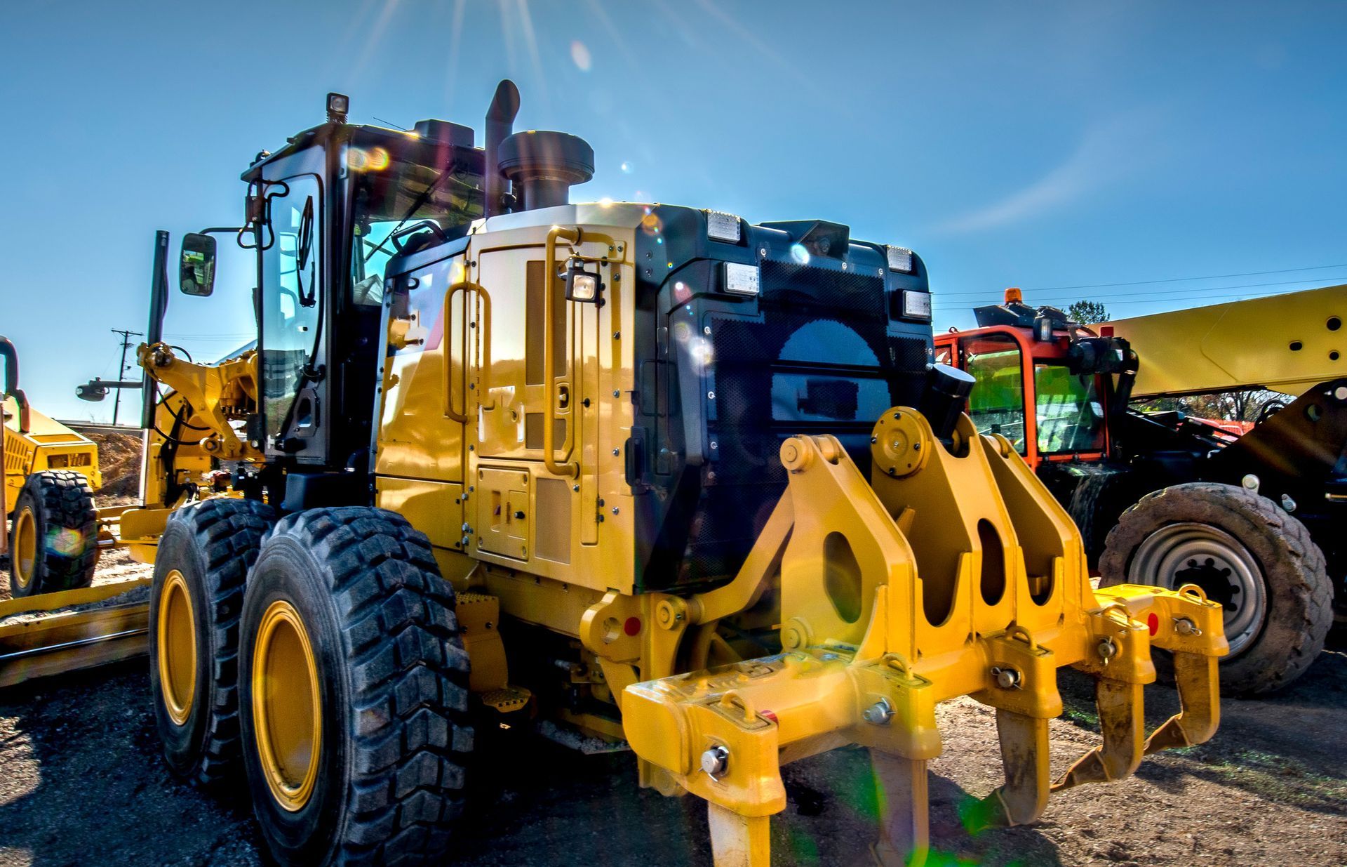 A yellow tractor is parked next to a black tractor on a dirt road.