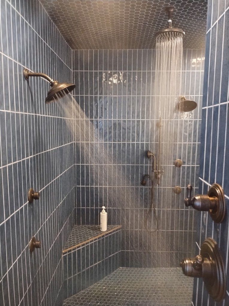 A shower with blue tiles and three shower heads.