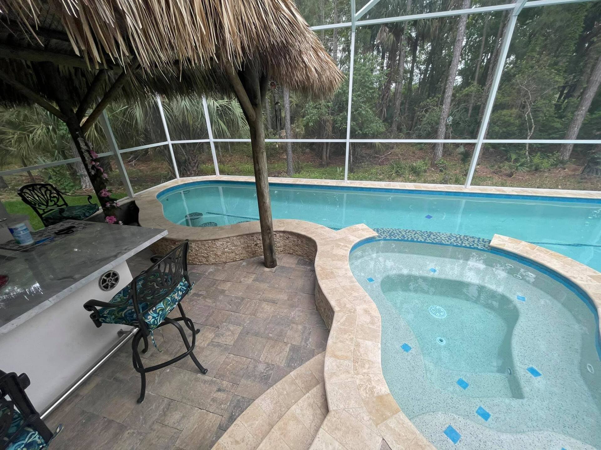 Tiki bar and hot tub beside a pool, set against a wooded background.