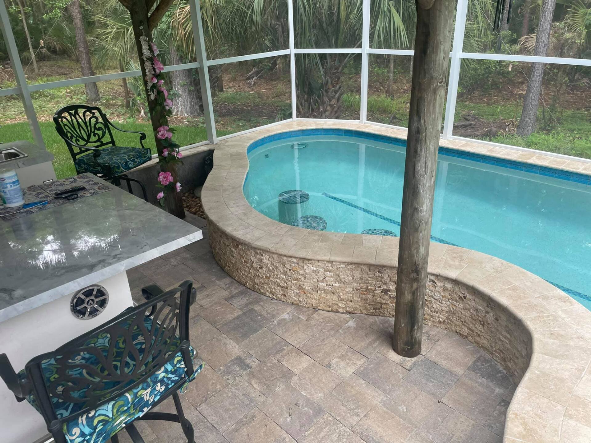 Pool area with a curved hot tub and bar seating. Stone and tile surround the pool.