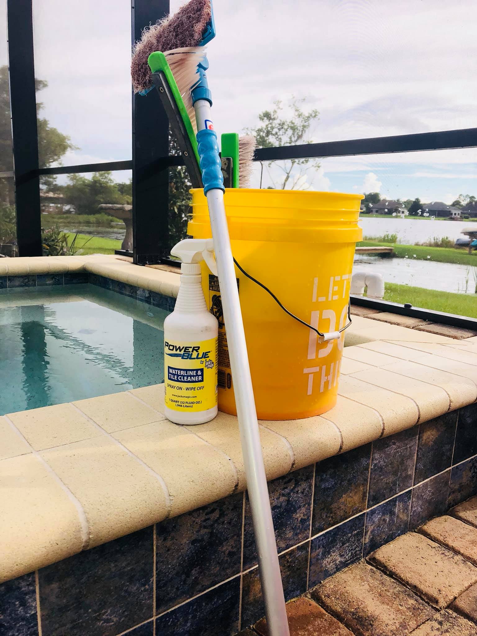 Cleaning supplies by a pool, including a bucket, spray bottle, and window cleaning tools.