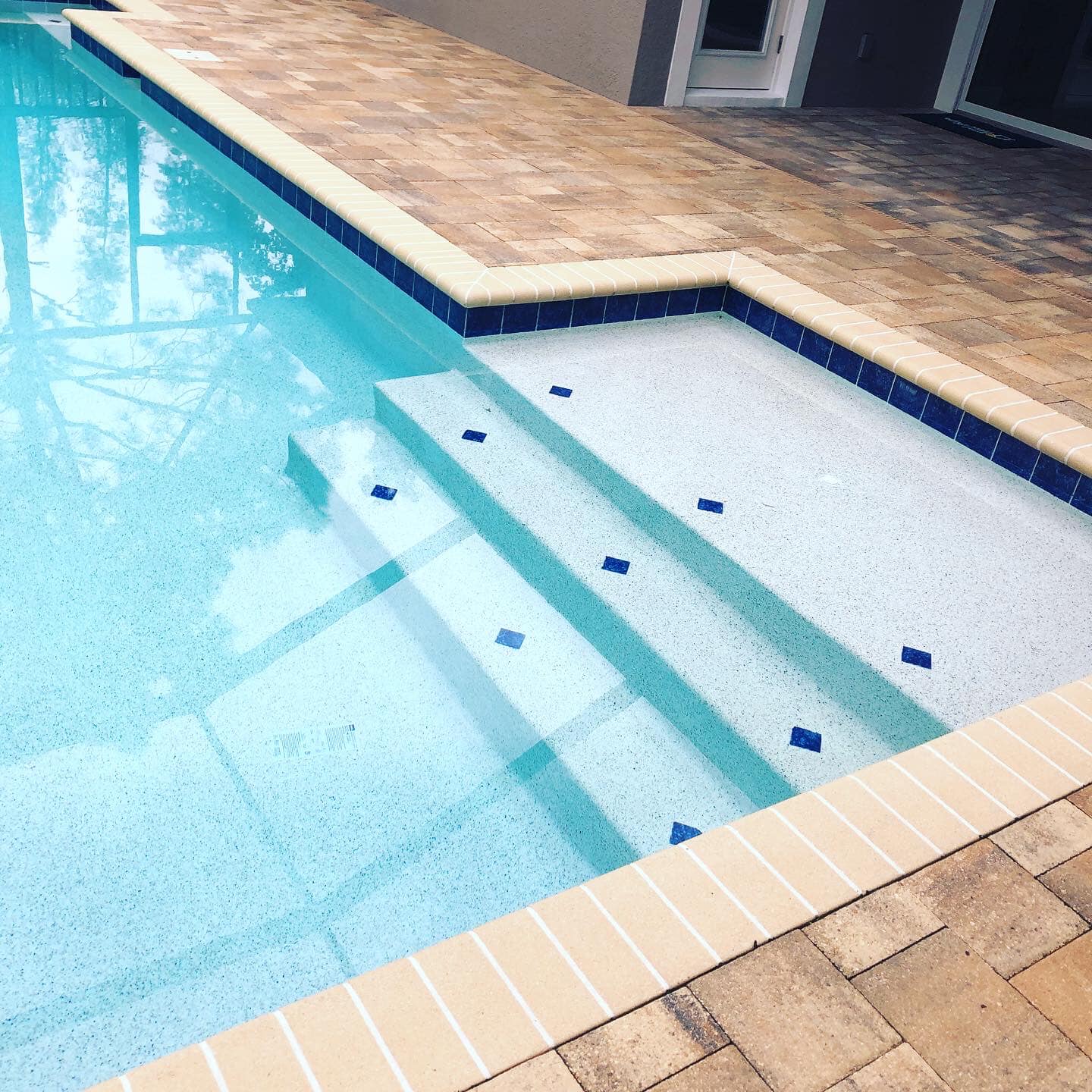 Swimming pool with blue water and steps, surrounded by light-colored tile.
