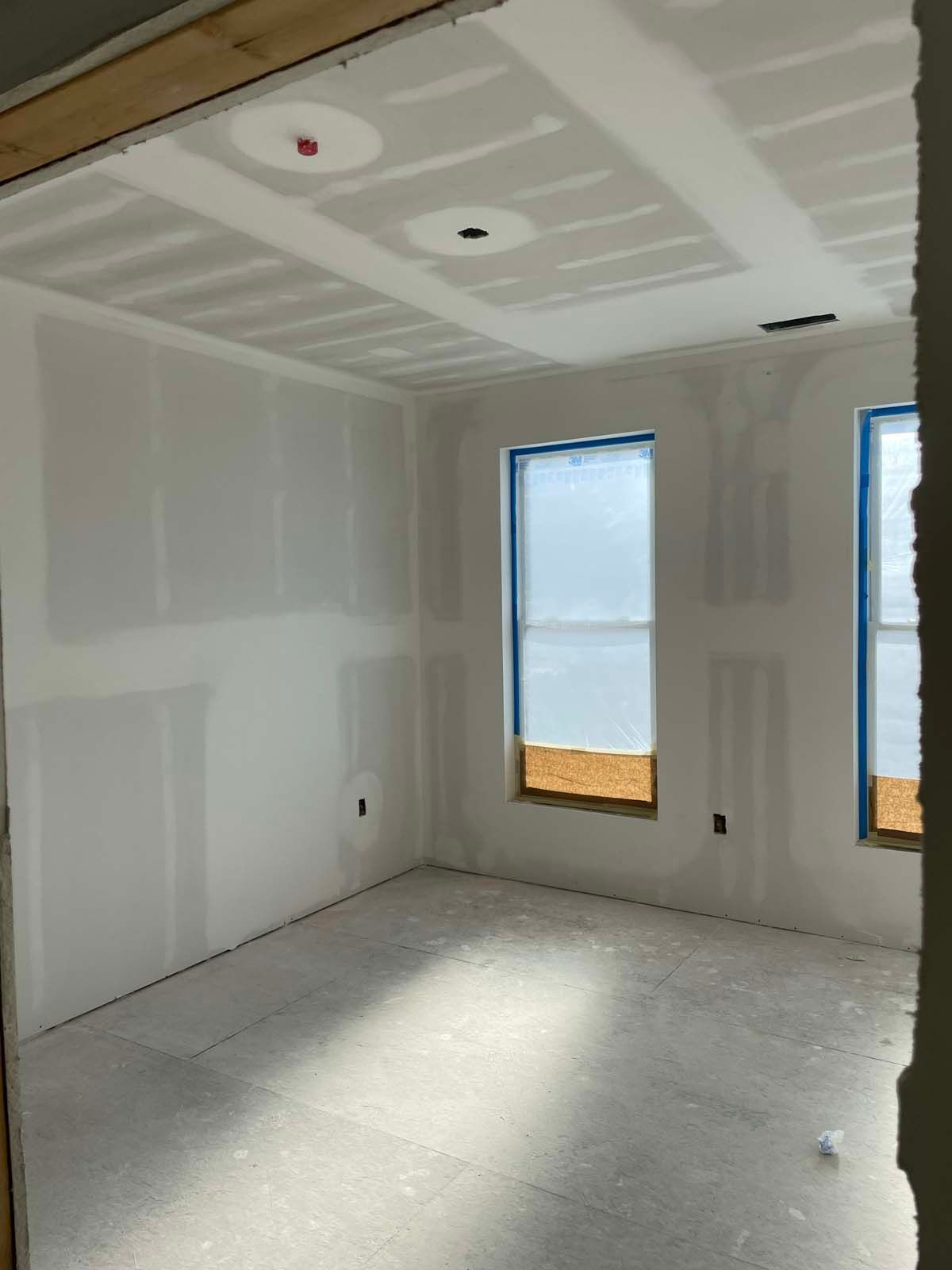Empty drywall room with unfinished ceiling, two windows, and sunlight on the floor