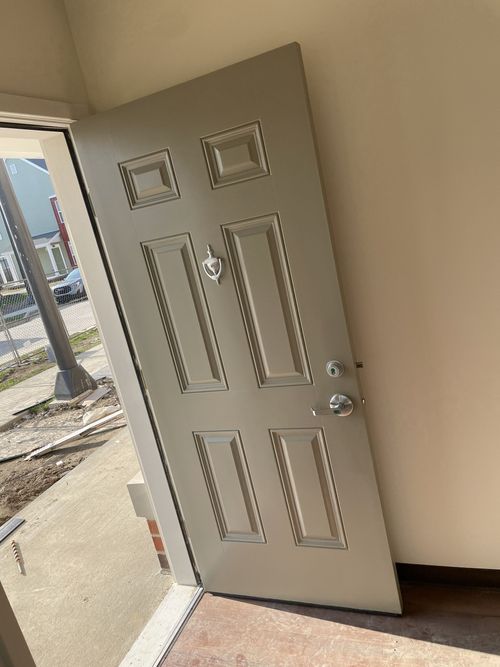 Open white front door inside a beige entryway, with outdoor construction visible outside.