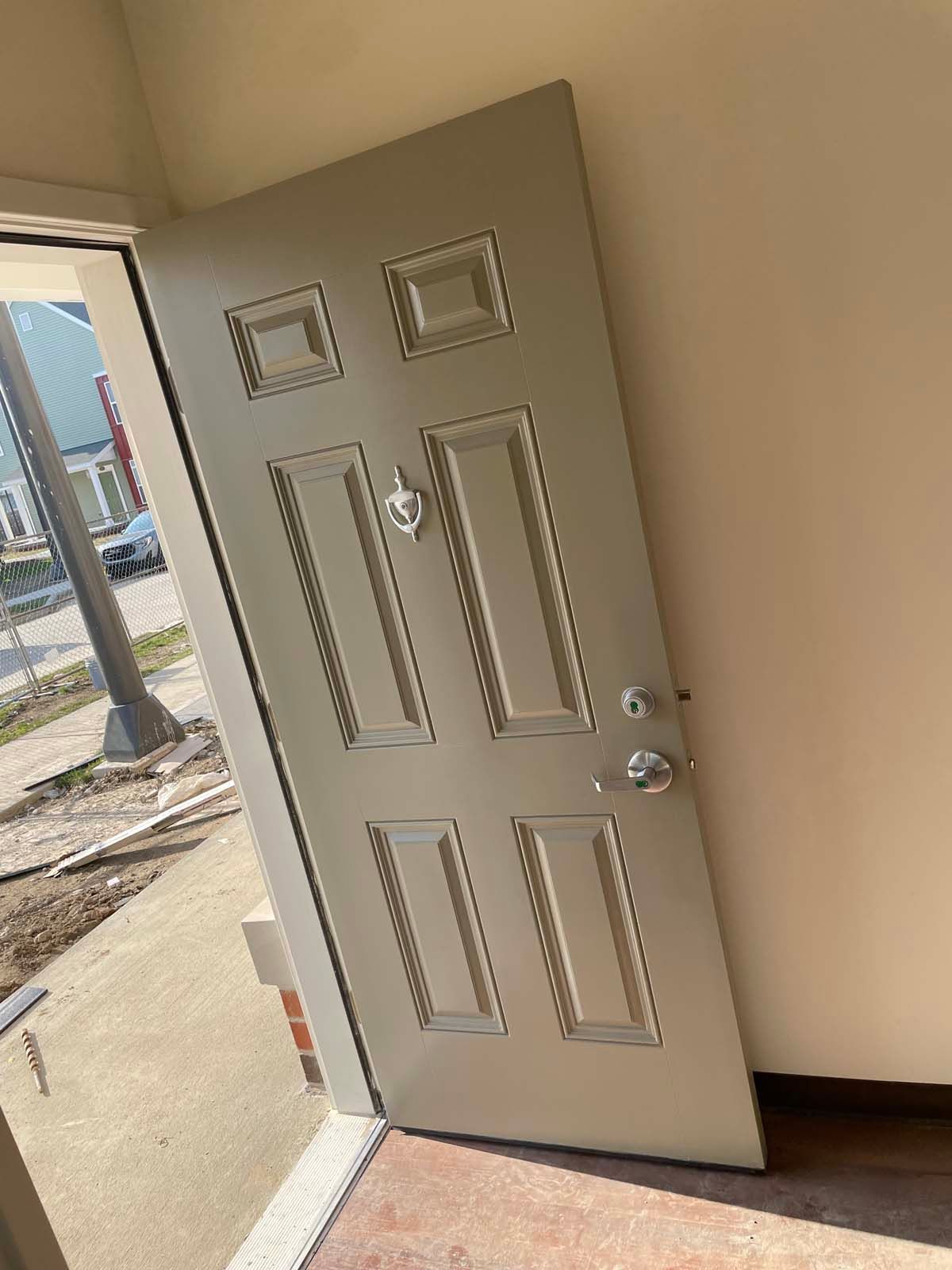 Open front door with small windows, leading outside to a sidewalk and street view.