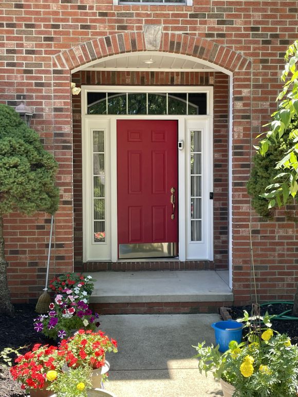 Brick house entry with a red front door, white trim, and colorful flowers in the foreground