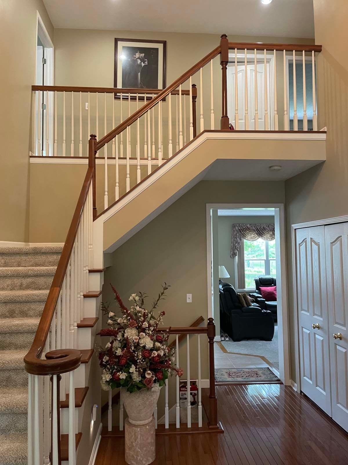 Interior foyer with staircase, white railing, hardwood floor, and a vase of flowers by the landing