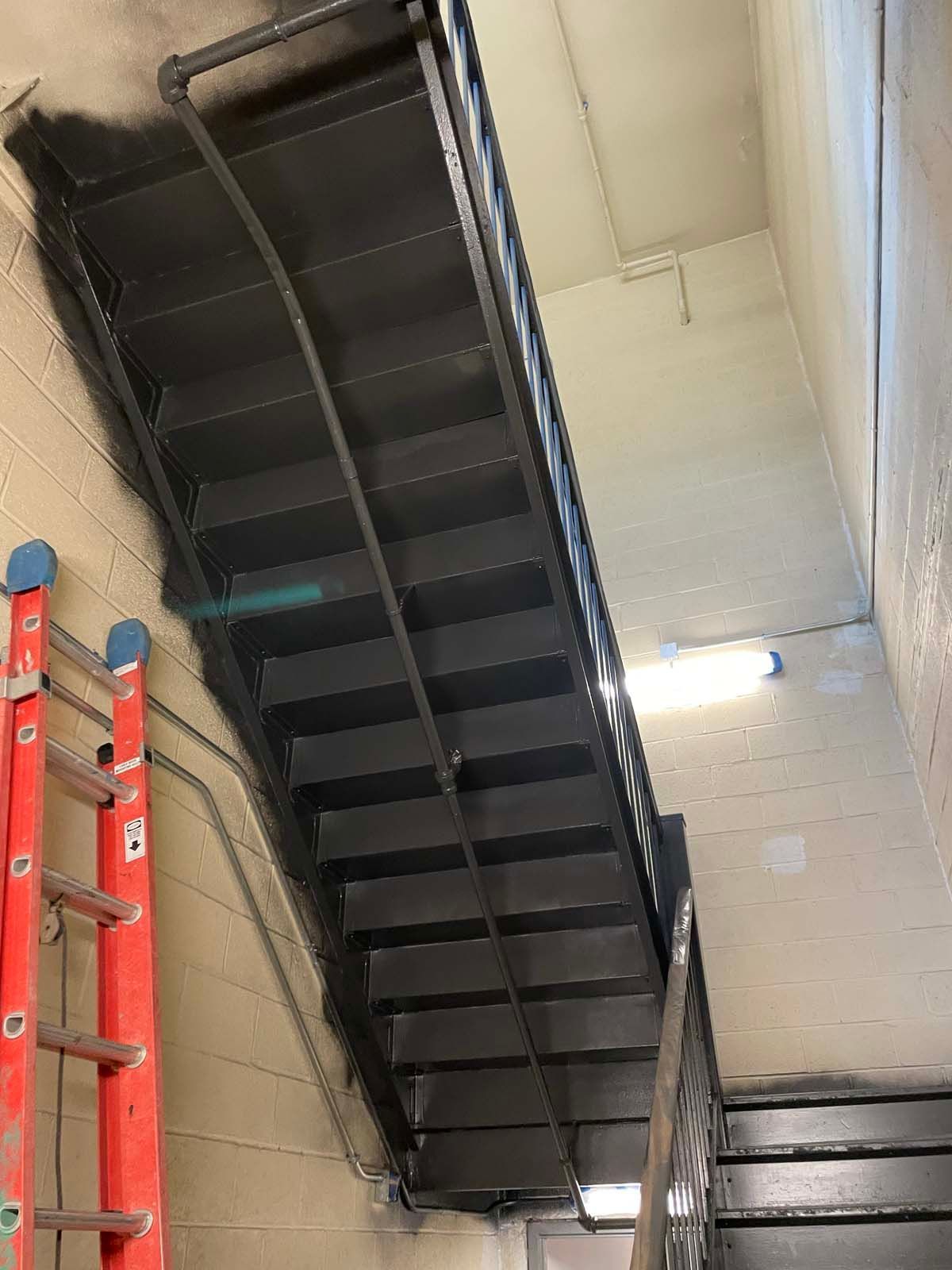 Black metal staircase/ladder viewed from below inside an industrial stairwell.