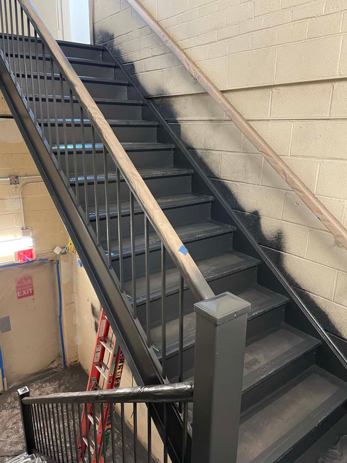 Basement stairwell with black metal stairs, railing, and boxes beside beige walls
