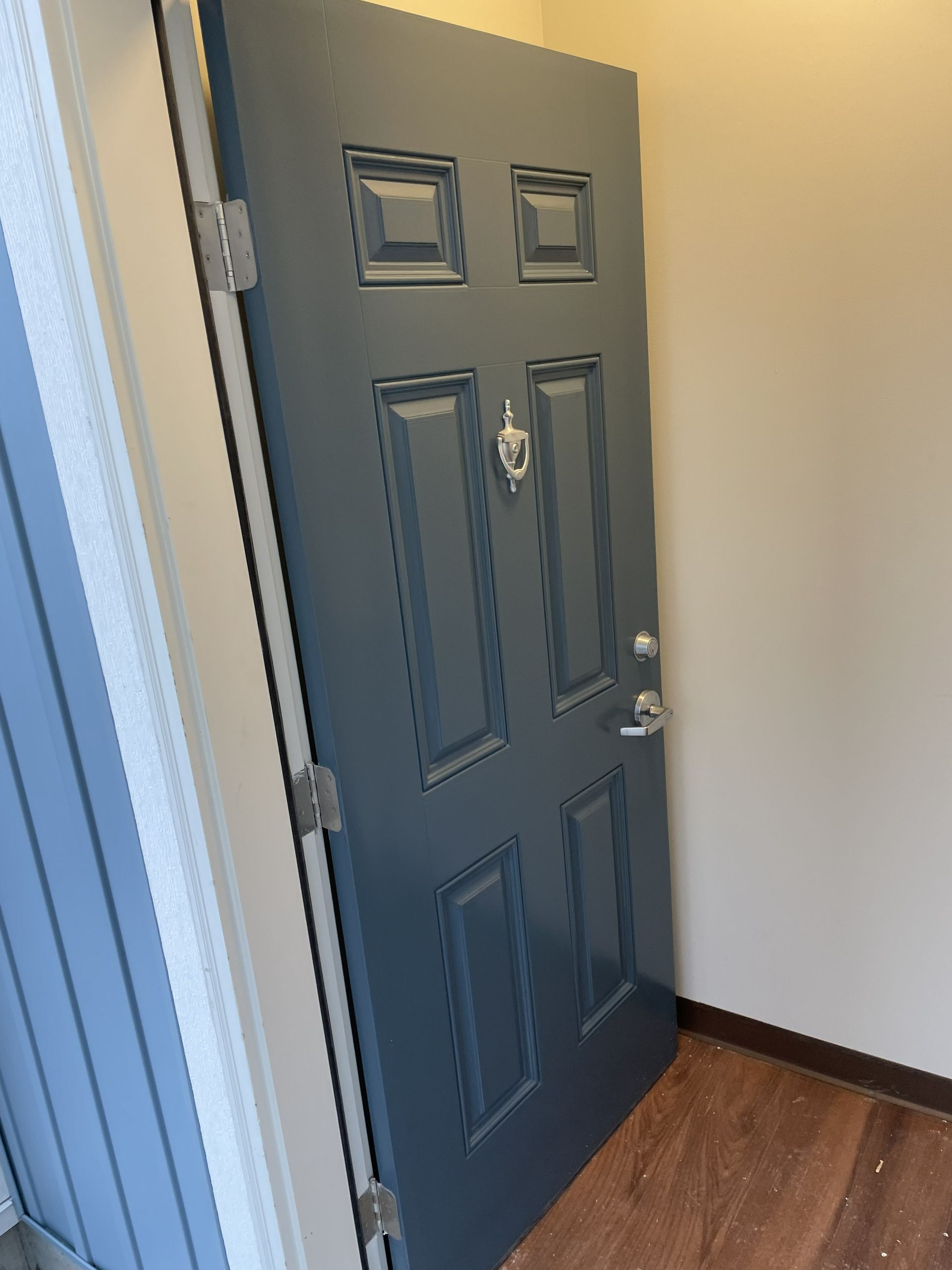 Open blue-gray front door with mail slot in a hallway, partially ajar.