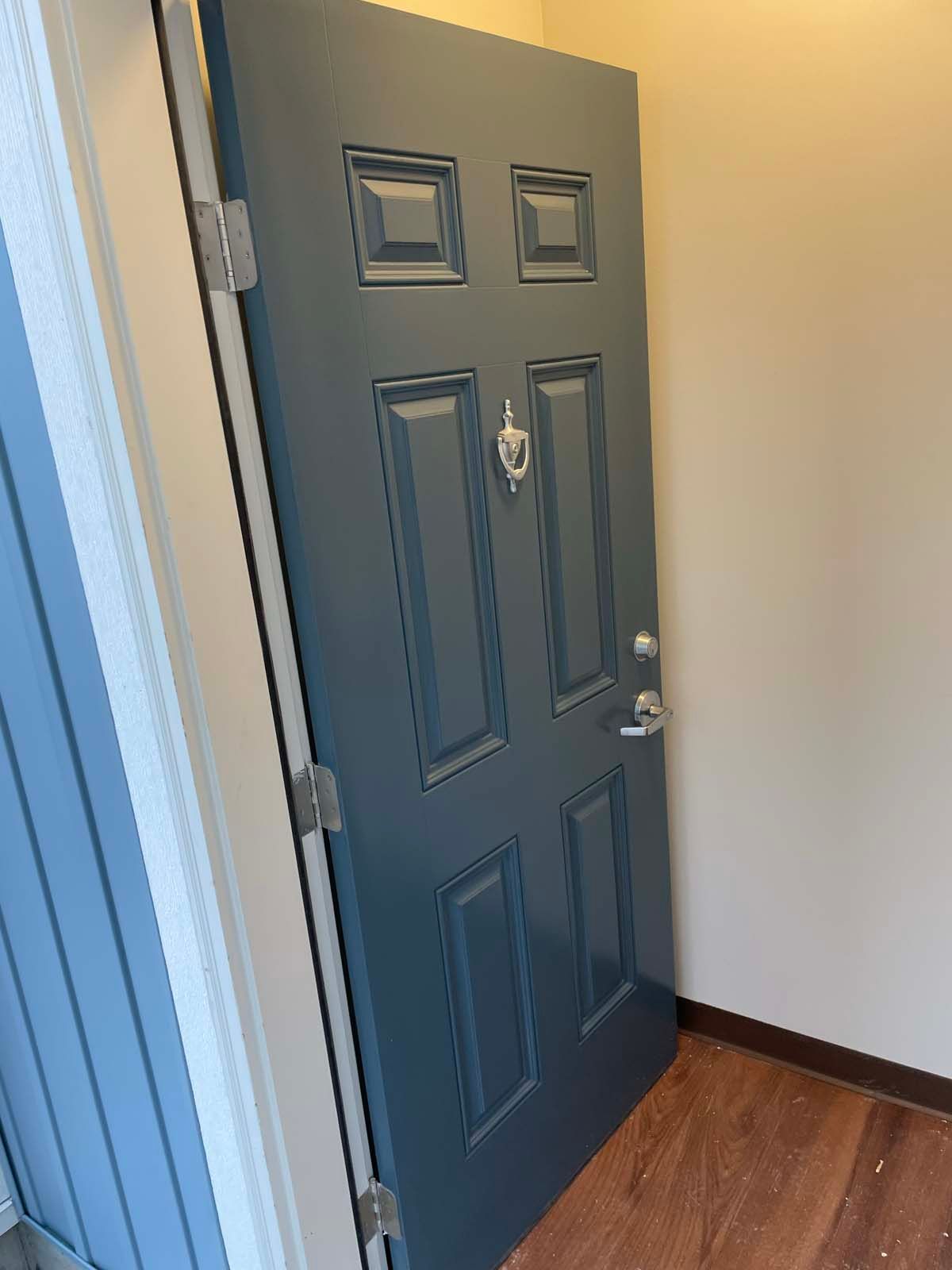 Open blue front door with peephole and silver knob in a hallway with wood flooring
