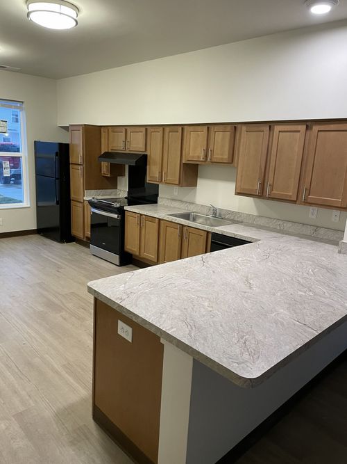 Empty kitchen with wood cabinets, granite countertops, stove, and light wood flooring.