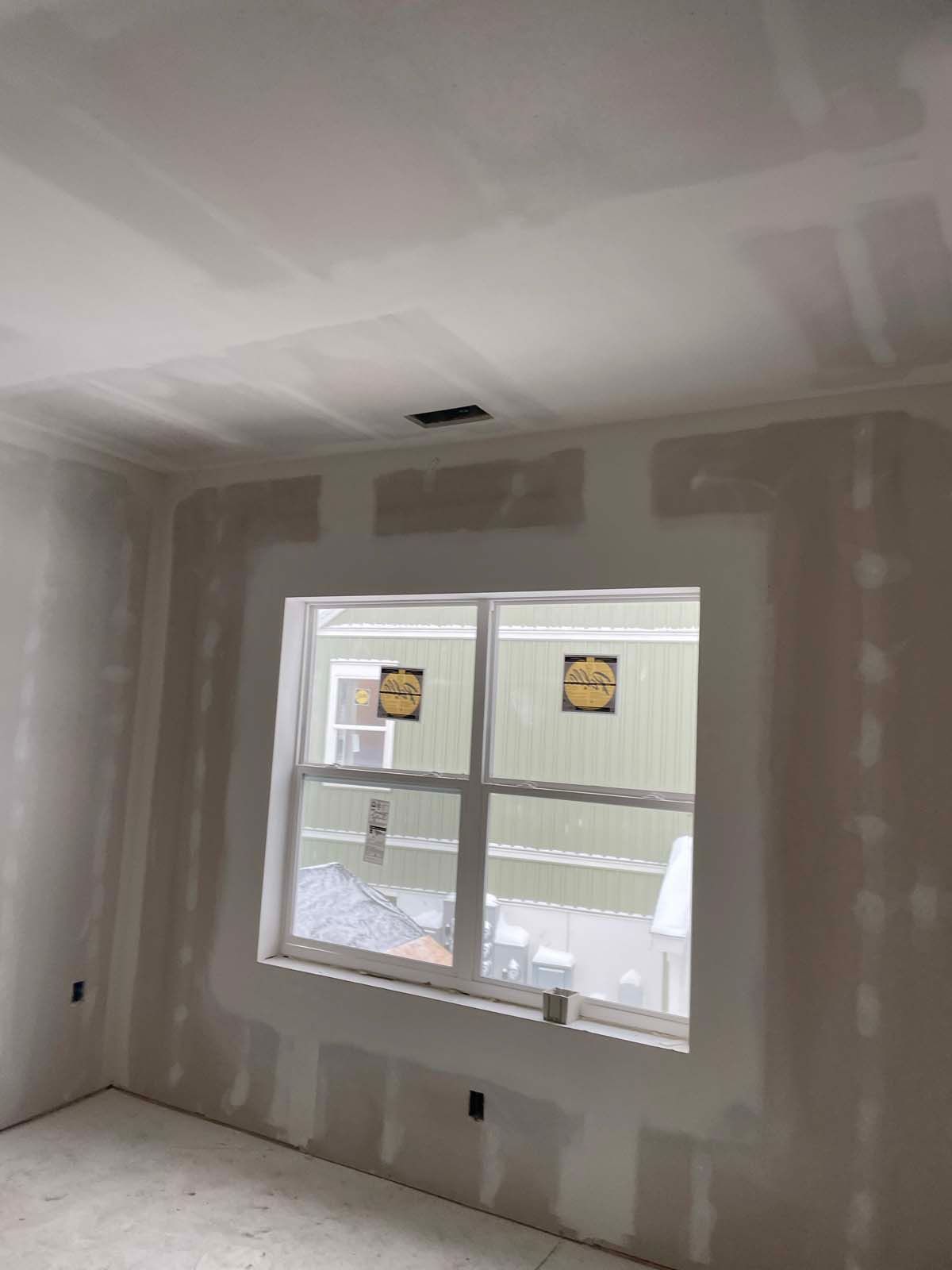 Empty unfinished room with drywall patches, a window, and white ceiling.