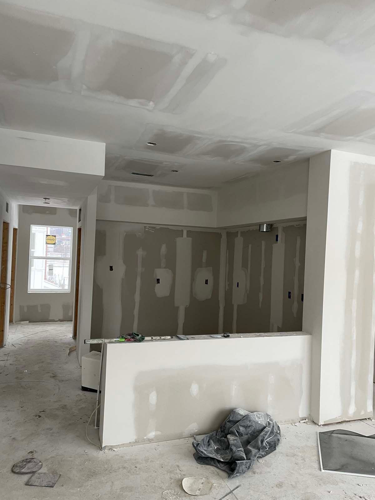 Unfinished room under construction with drywall, exposed ceiling, window, and debris on the floor