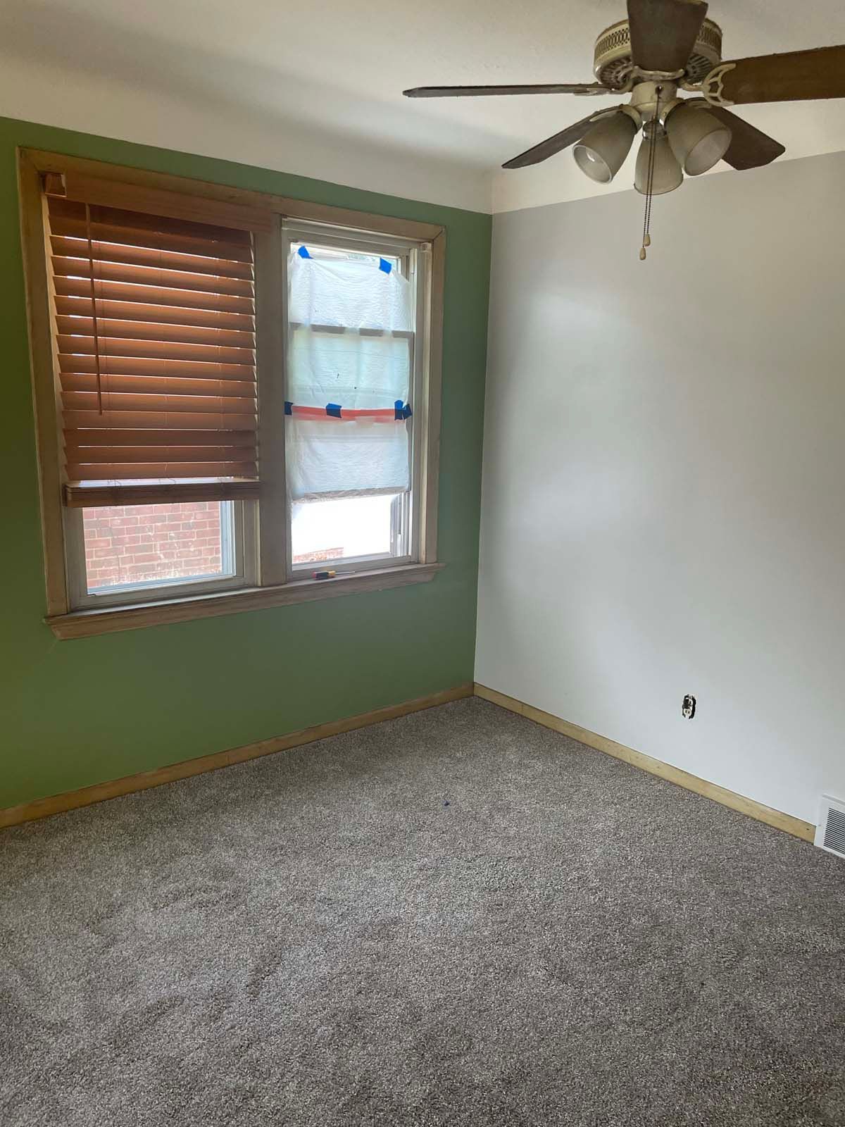 Empty bedroom with green walls, carpeted floor, window blinds, and a ceiling fan.