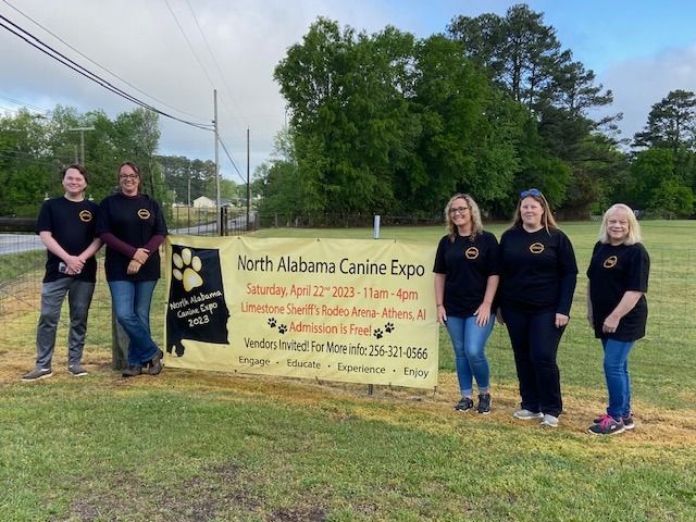 A group of women and men standing in front of a sign that says north Alabama canine expo