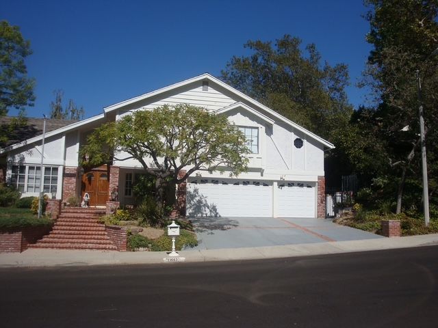 Two-story white house with brick accents, three-car garage, and a tree in front, on a sunny day.