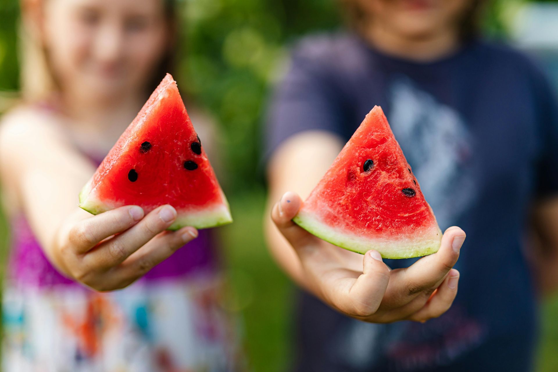 A boy and a girl are holding slices of watermelon in their hands.