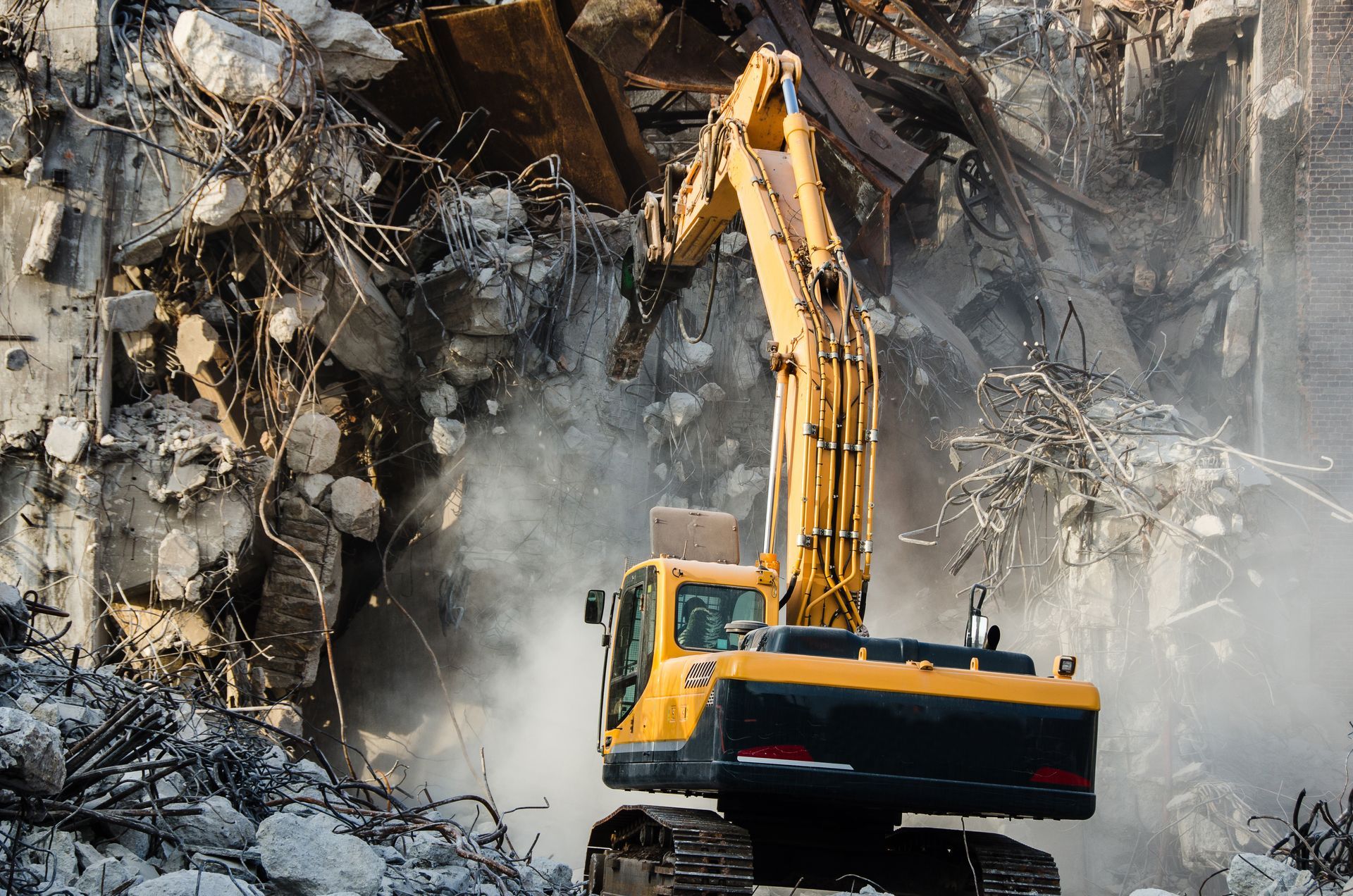 Yellow excavator demolishing a rubble-strewn wall amid dust and debris