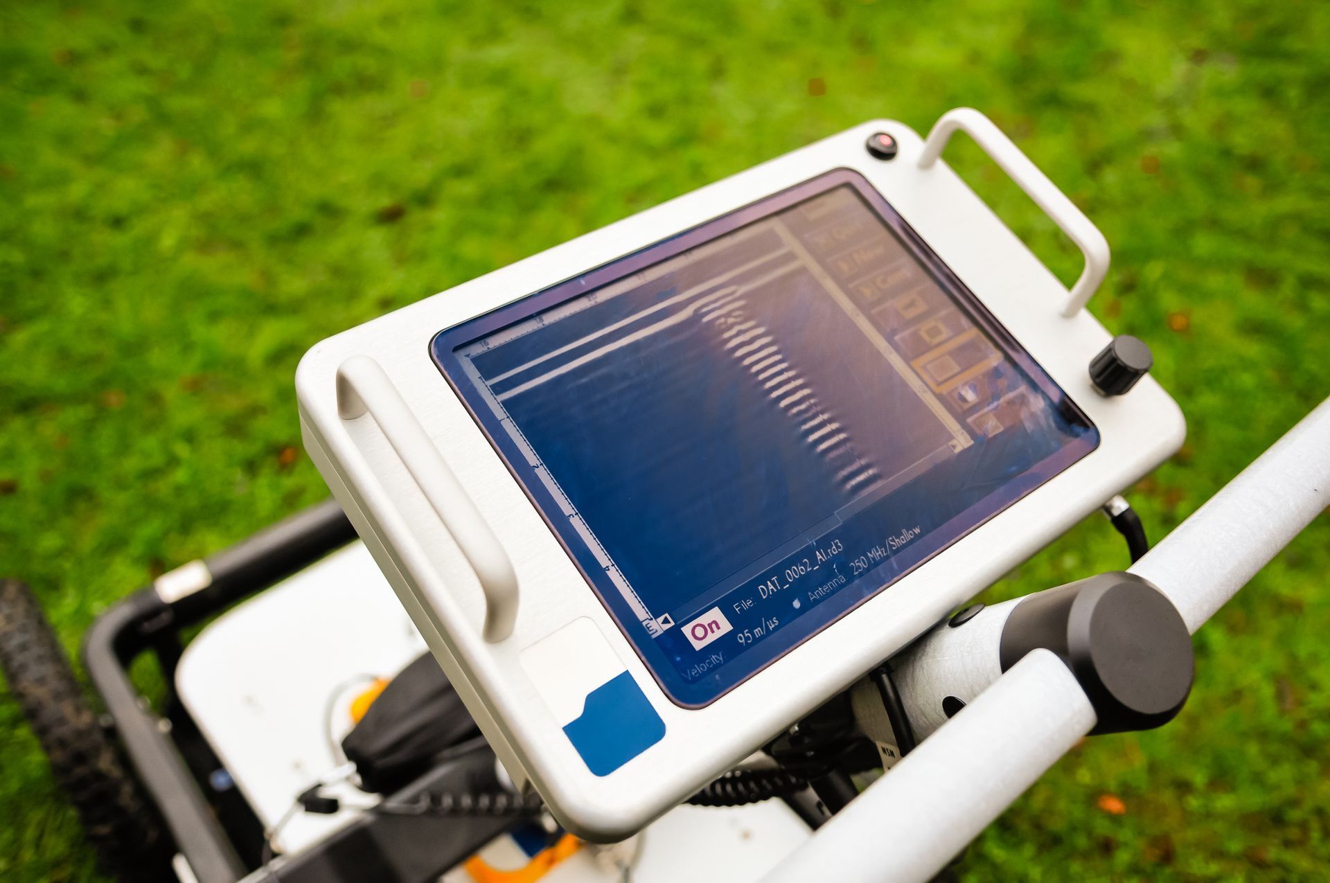A ground-penetrating radar mounted on wheels, used to survey below grass-filled ground.