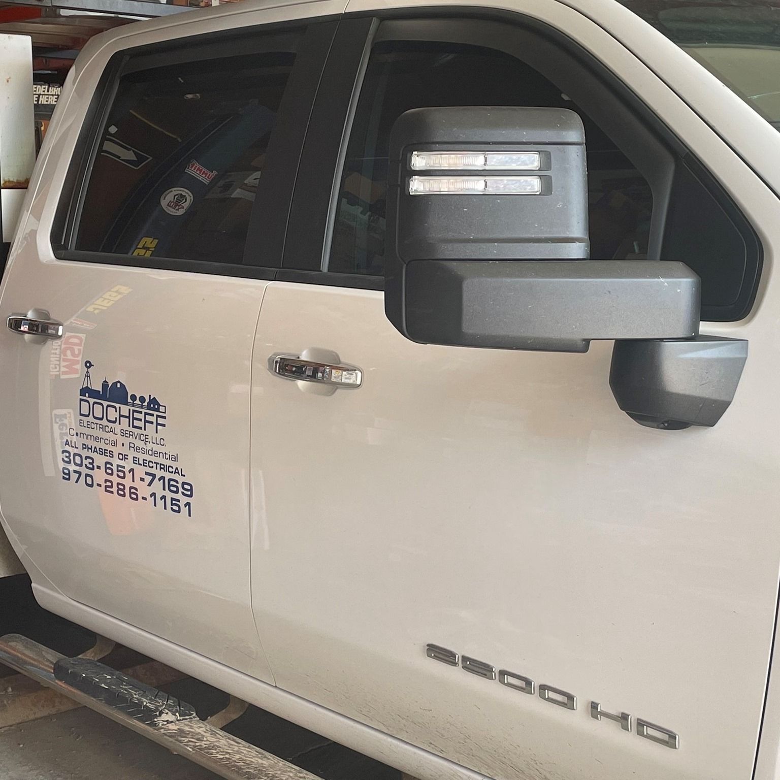 White GMC HD pickup truck parked indoors with business decals on the door and side mirror visible.