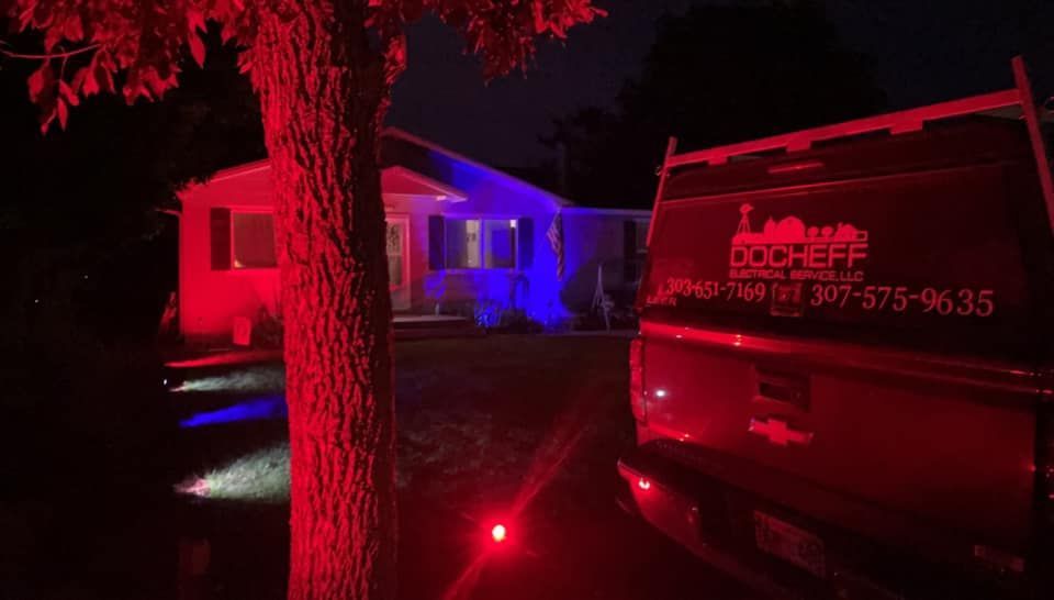 Red-lit house exterior at night with a tree in front and a parked utility truck on the right.