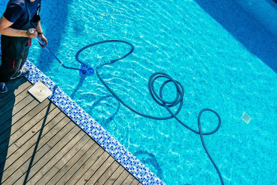 Pool professional skimming leaves from a backyard pool.