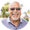 Smiling man with glasses and gray goatee in a light blue polo shirt, outdoors against a blurred background