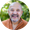 Smiling bald man in an orange jacket outdoors with a blurred green background