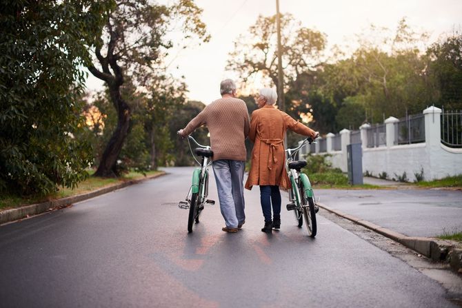 Two people walking bicycles down a tree-lined road at sunset