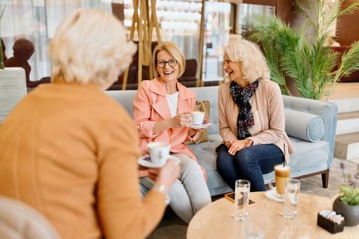 Three people chatting in a bright lounge, holding coffee cups around a low table