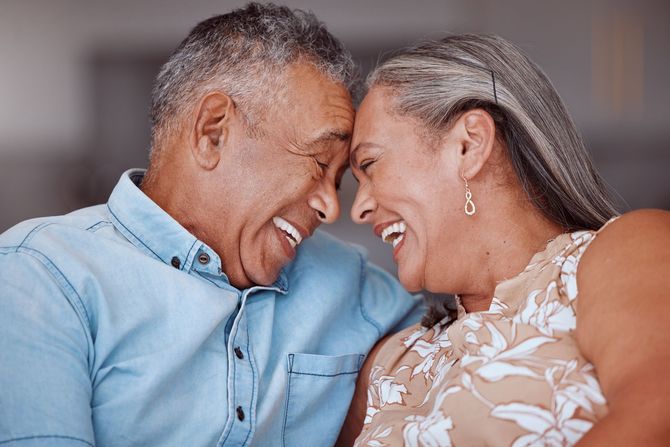 Two smiling people leaning forehead to forehead in a warm, intimate pose