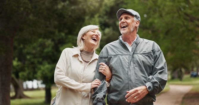 Smiling couple walking arm in arm along a tree-lined park path