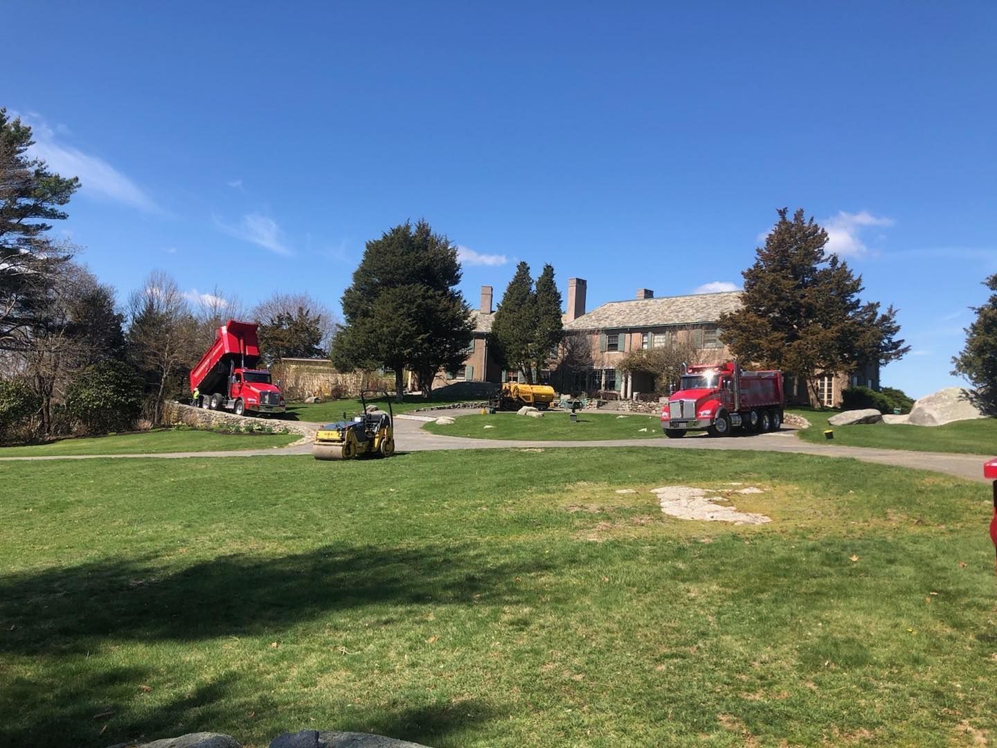 Two red dump trucks are parked in front of a large house.