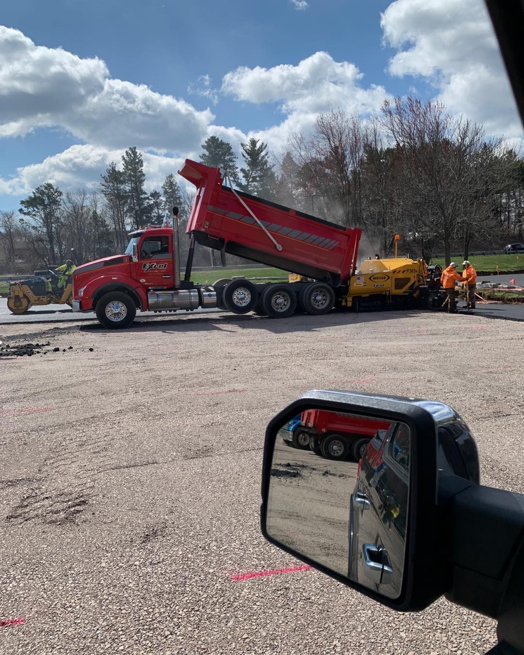 A dump truck is being loaded with gravel in a parking lot.