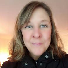 A woman in a black jacket is smiling for the camera.